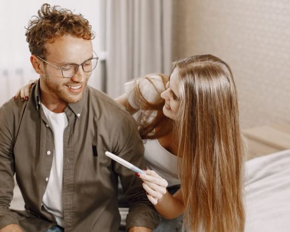 Joyful couple sitting on bed, holding a pregnancy test, embracing new beginnings.